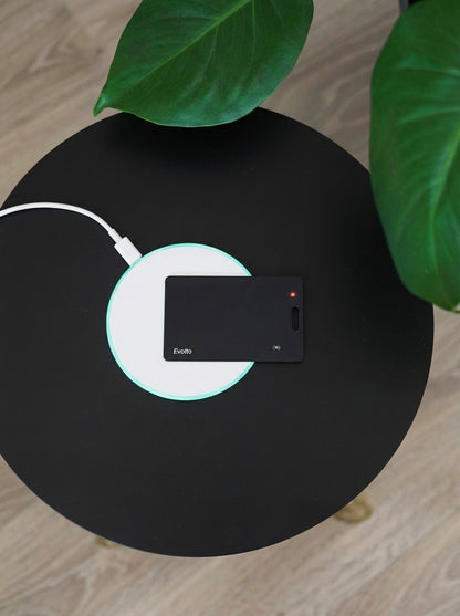 Svart Evolto tracking card som laddas på en rund, vit trådlös laddare med en lysande grön ring.